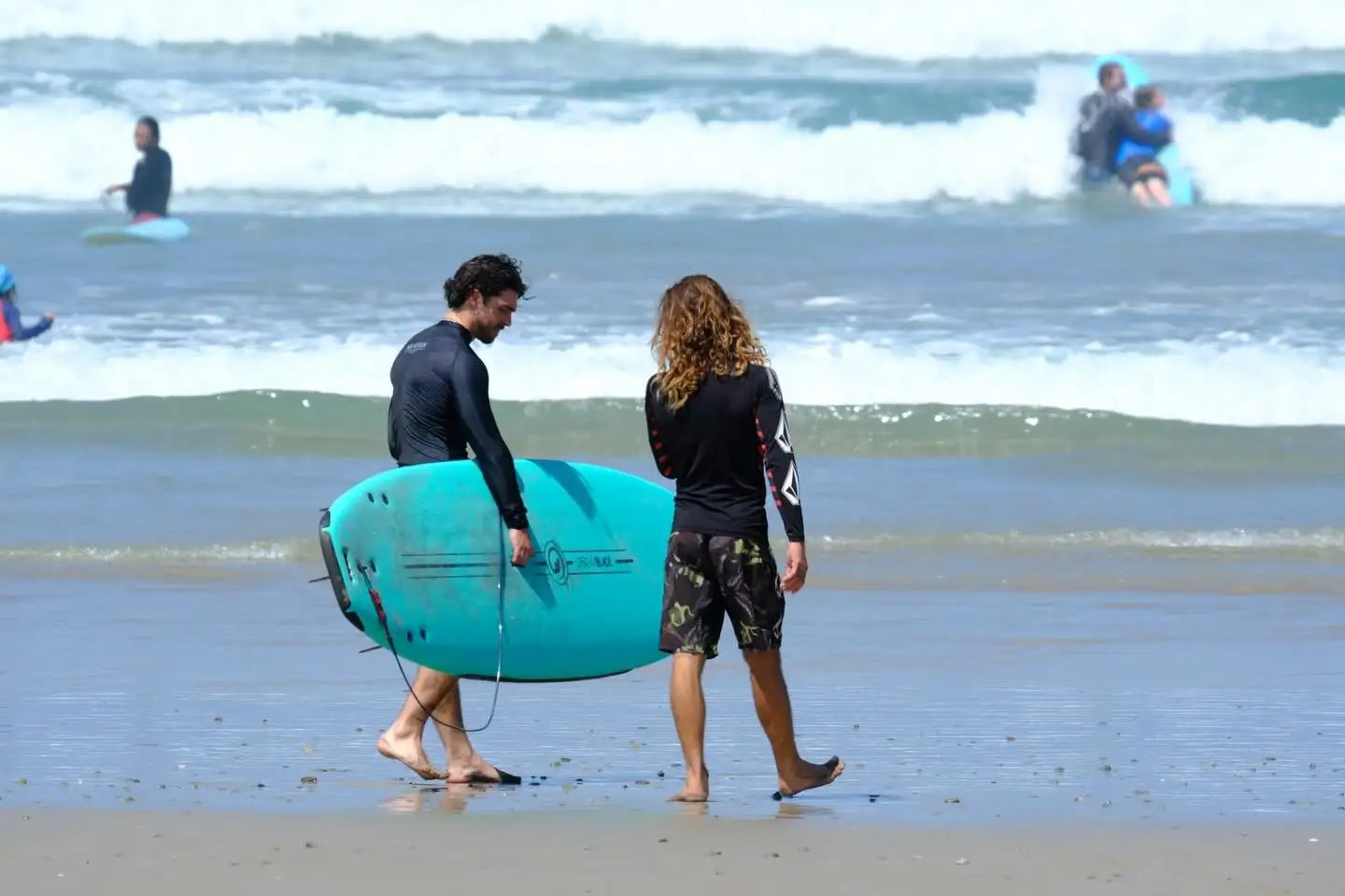 Instructor and student walking to the water with a soft-top board
