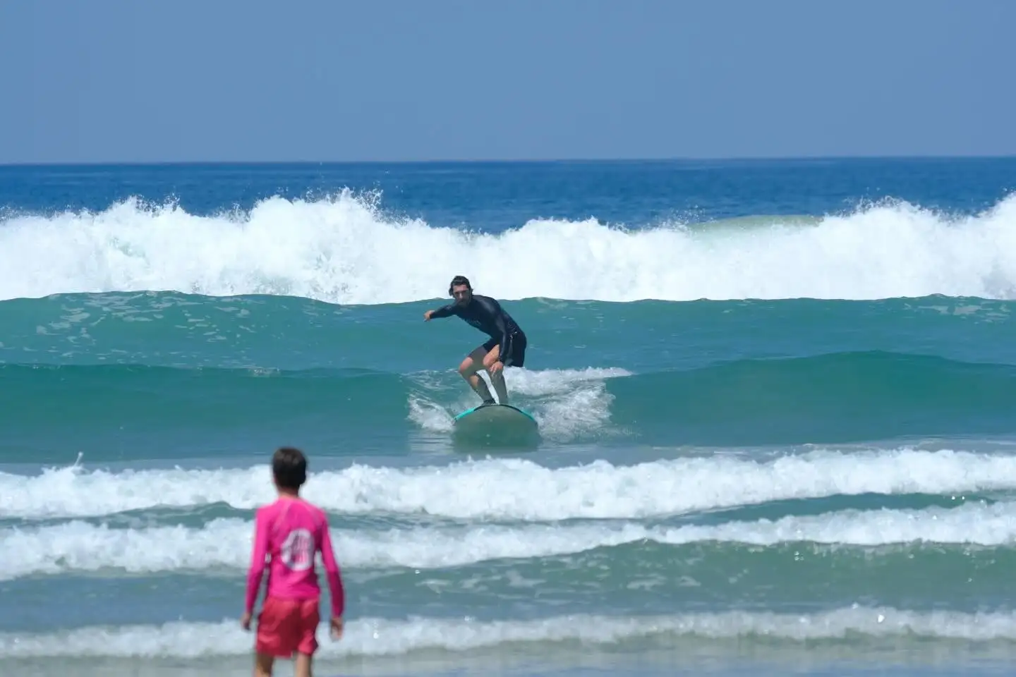 Surfer catching a wave during a lesson in Santa Teresa while a young student watches