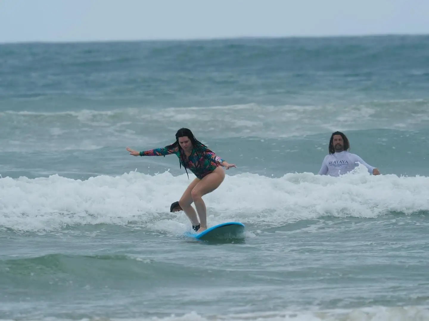Woman standing up on her board in the whitewater while her instructor watches
